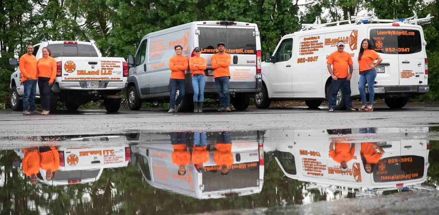 A group of people standing in front of three work vehicles, all branded with orange logos and text, reflecting in a puddle on the ground.