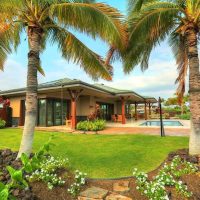 A modern house surrounded by palm trees and lush greenery, with a swimming pool visible in the backyard.