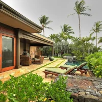 A luxurious outdoor patio area with lounge chairs, surrounded by lush greenery and palm trees, leading to a pool.
